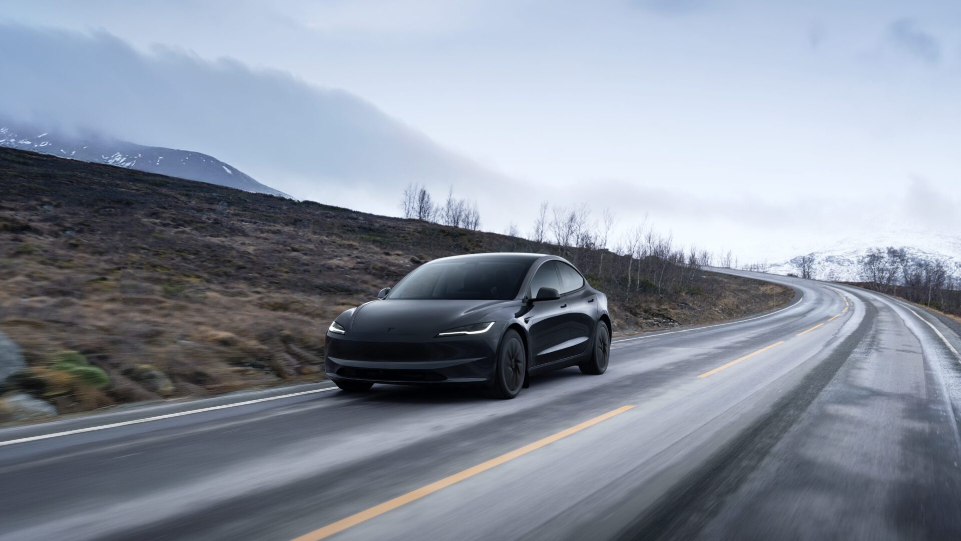 Dark gray Tesla Model 3 Highland driving on a mountain road