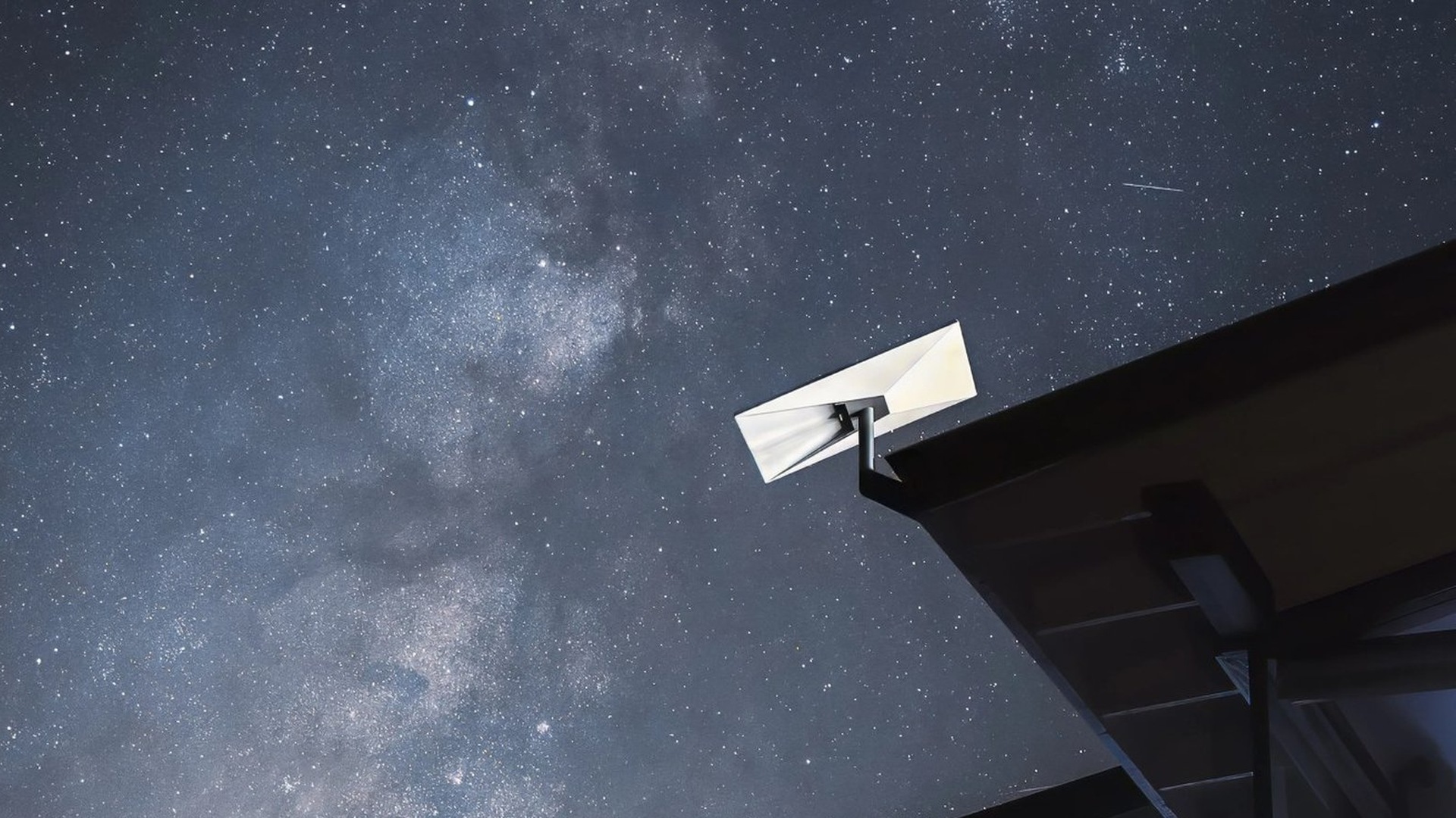 featured-1920x1080 | TeslaNorth.com White Starlink dish mounted on a dark rooftop under a starry night sky with the Milky Way
