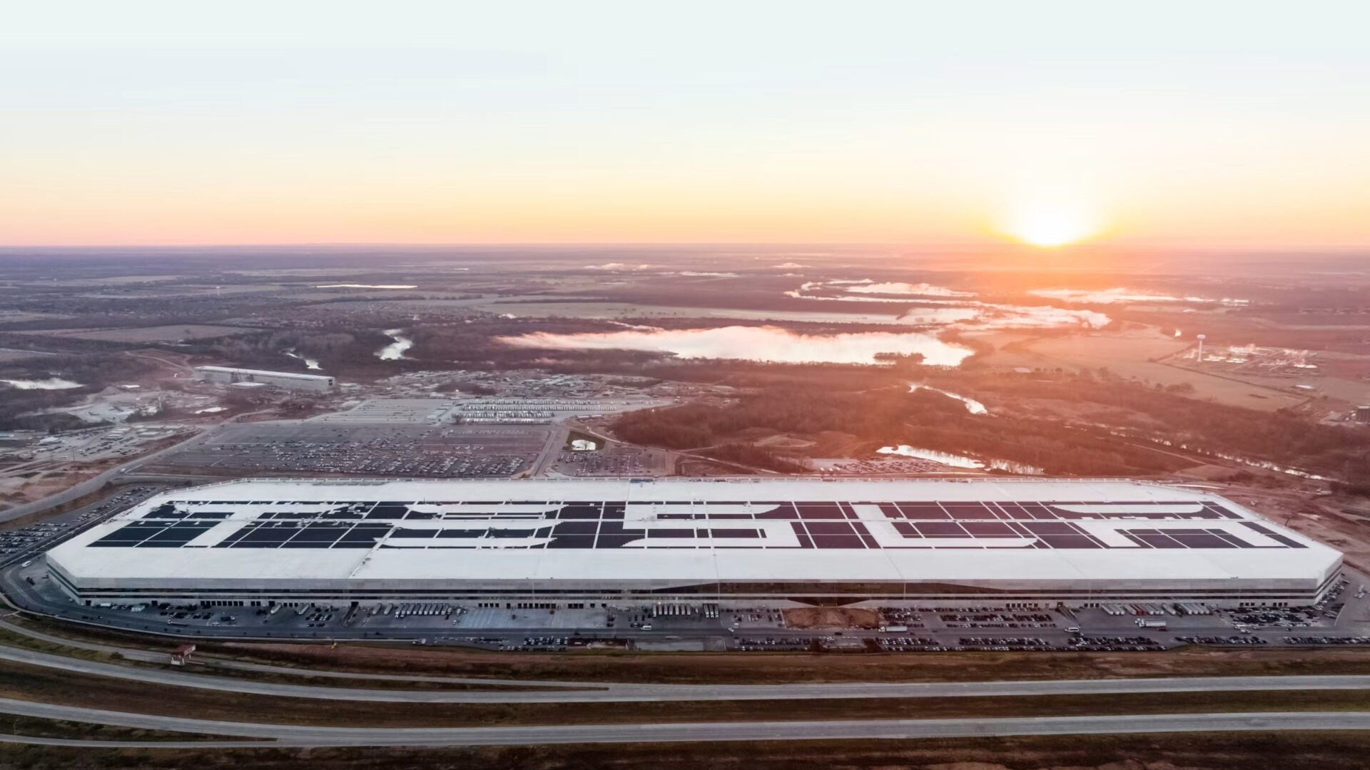 Aerial view of Gigafactory Texas with TESLA spelled out in solar panels on the roof at sunrise