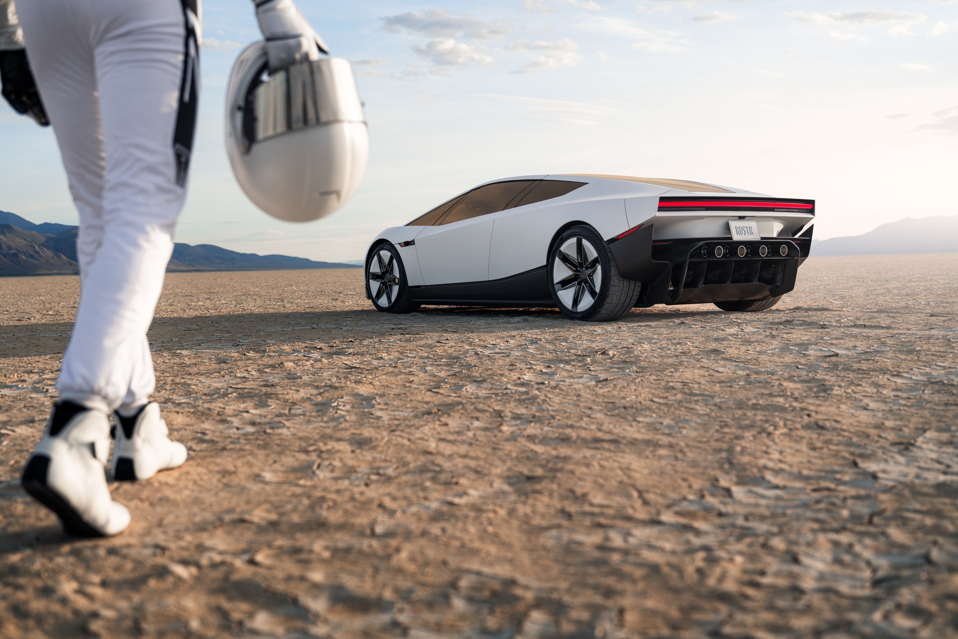 Tesla Roadster on a dry lakebed with a helmeted driver in a white suit walking toward it