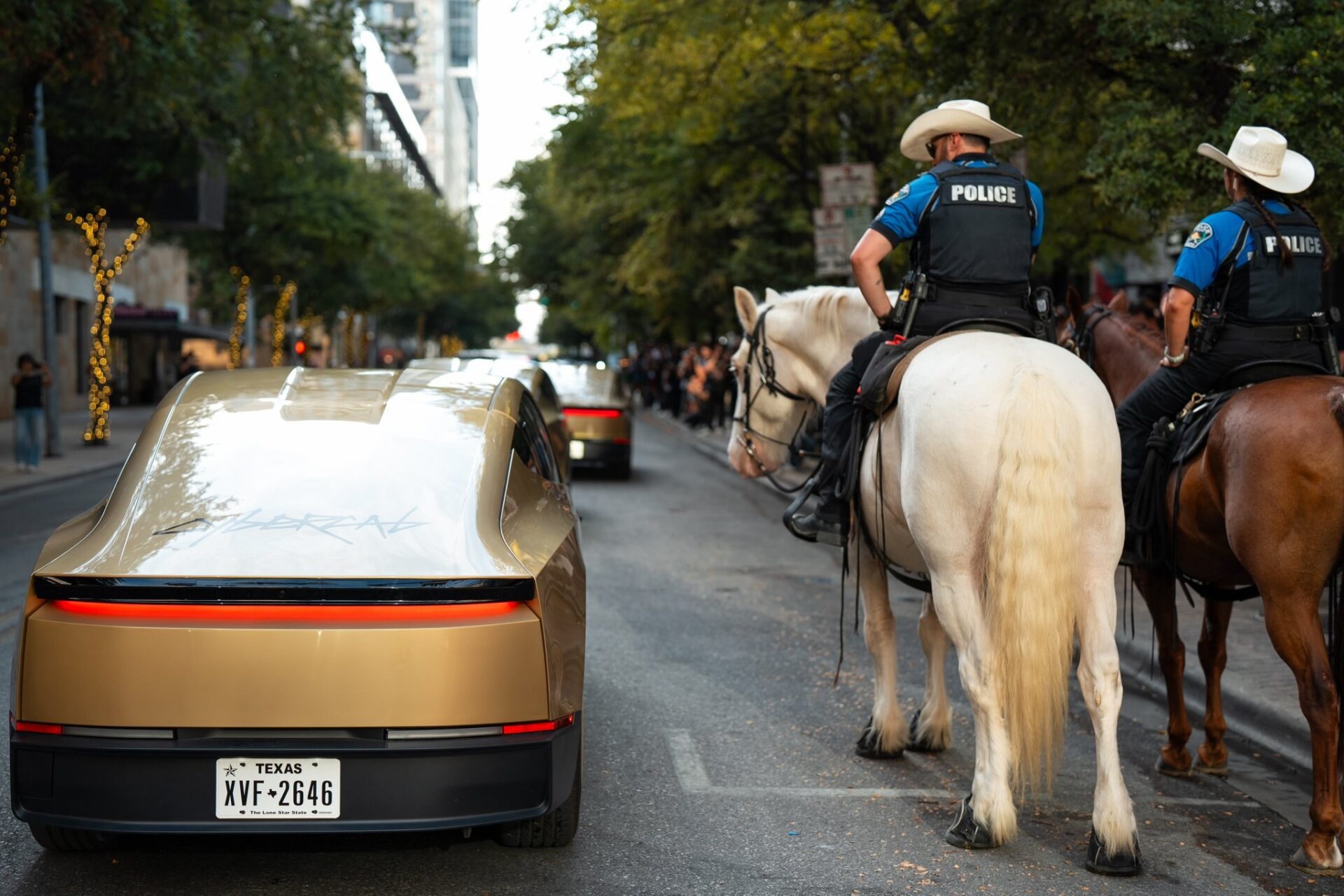 A gold Tesla Cybercab on a downtown Austin street beside two mounted police officers