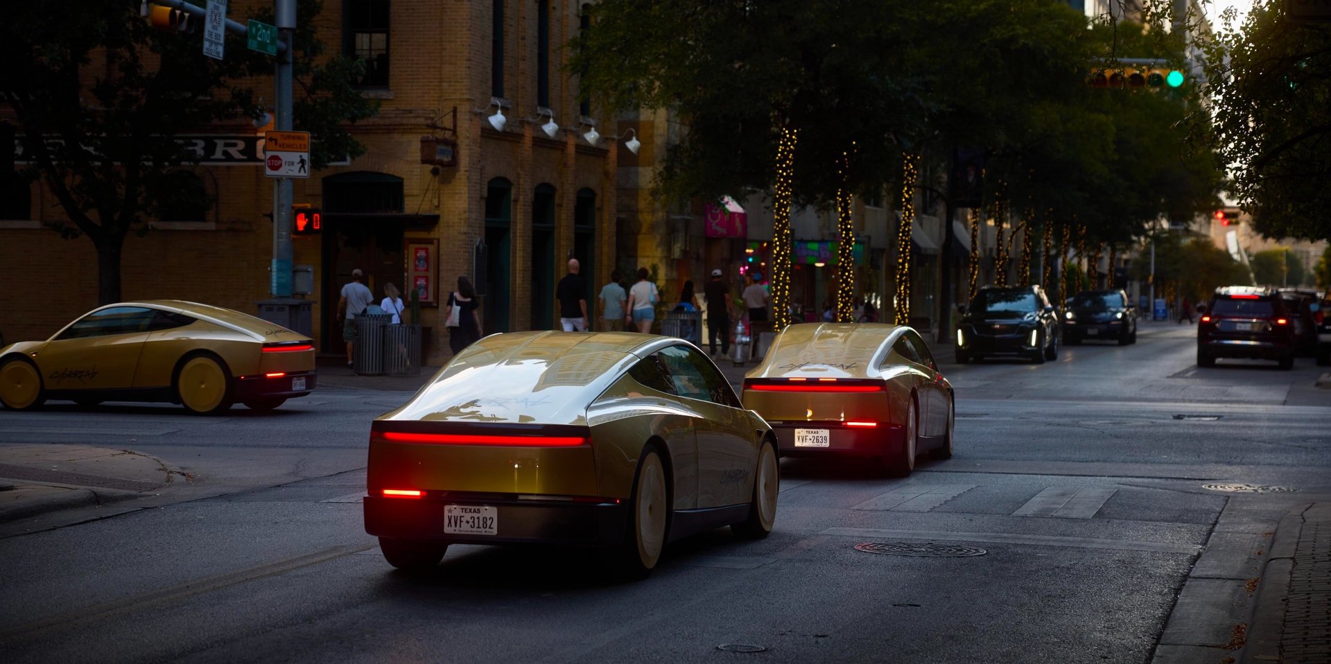 Three gold Tesla Cybercabs driving on a downtown Austin street at dusk, seen from behind with their taillights on.
