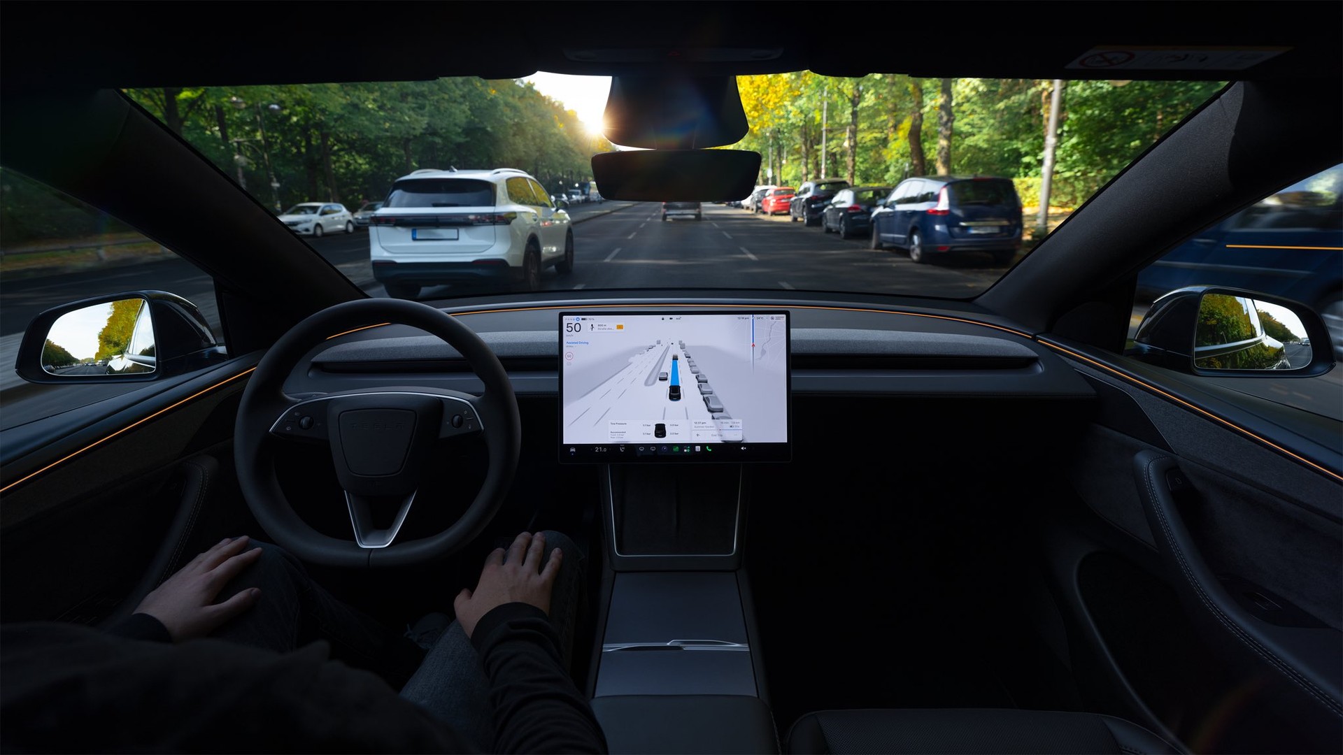 View from the driver's seat of a Tesla on a tree-lined road, with the driving visualization on the touchscreen