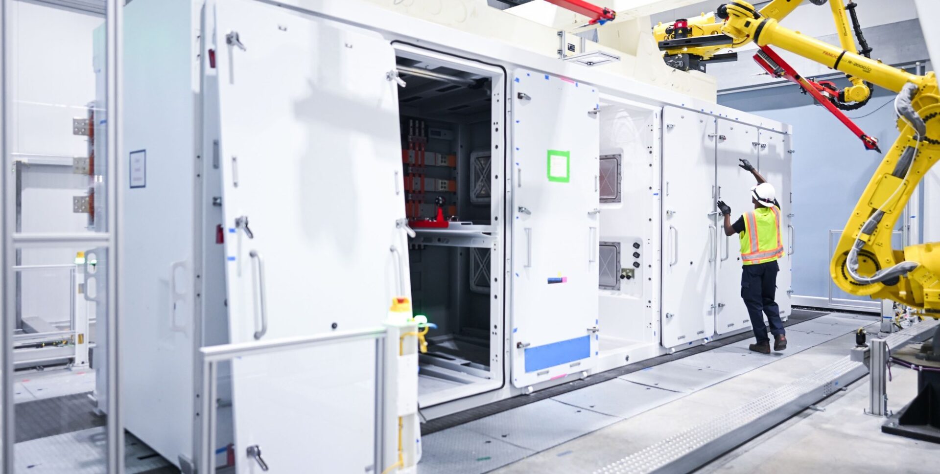 Worker inspecting a Megapack unit beside robotic arms at Tesla's Megafactory Texas