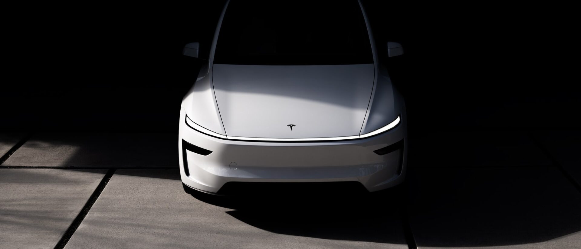 White Tesla Model Y parked on a concrete floor in a dim garage
