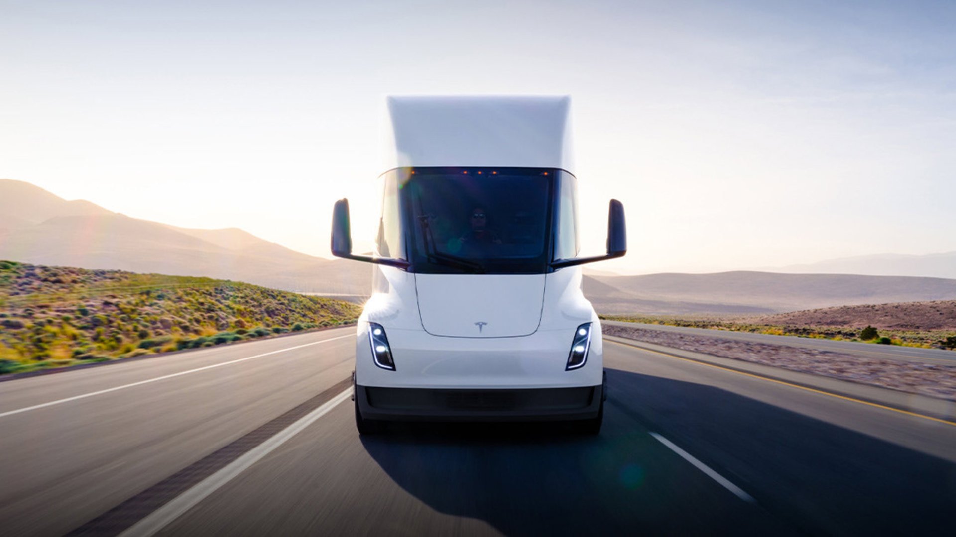 White Tesla Semi truck driving toward the camera on a highway at sunrise